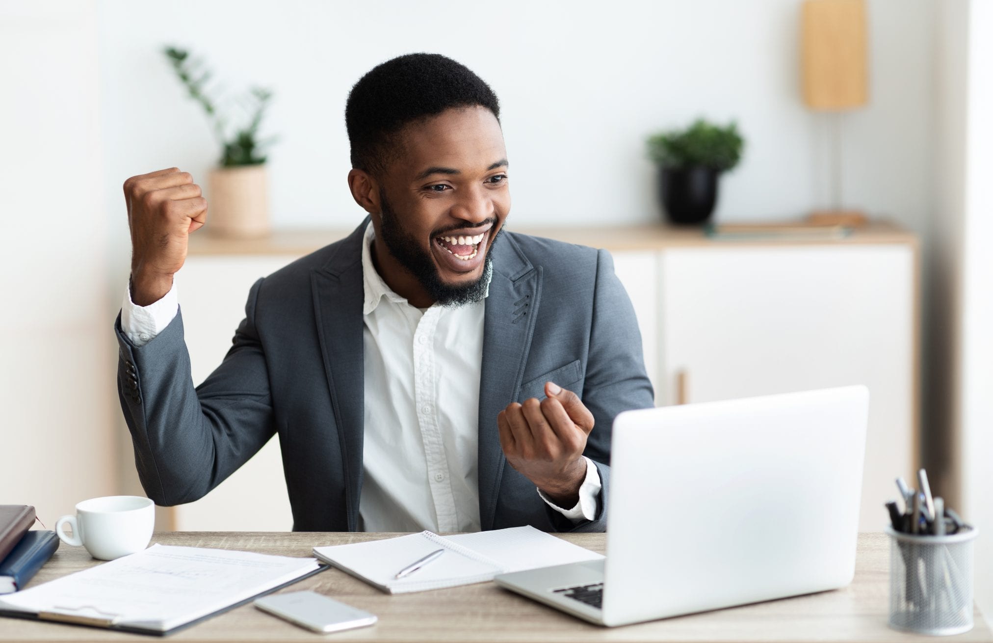 Happy black businessman rejoicing success at workplace in office