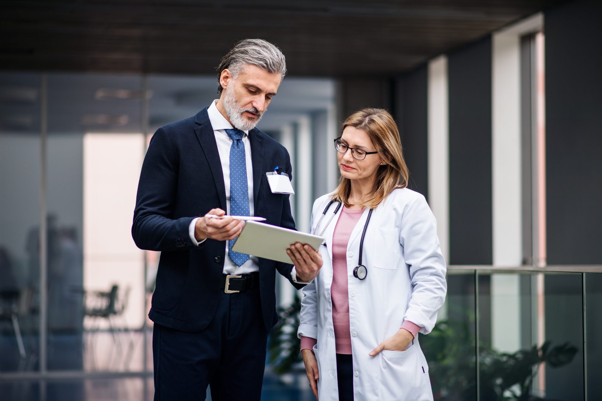 Pharmaceutical sales representative with tablet talking to woman doctor.